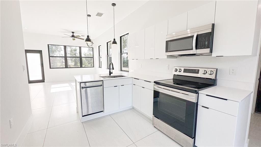Modern kitchen featuring white cabinetry, stainless steel appliances, a center island with sink, and white tile flooring