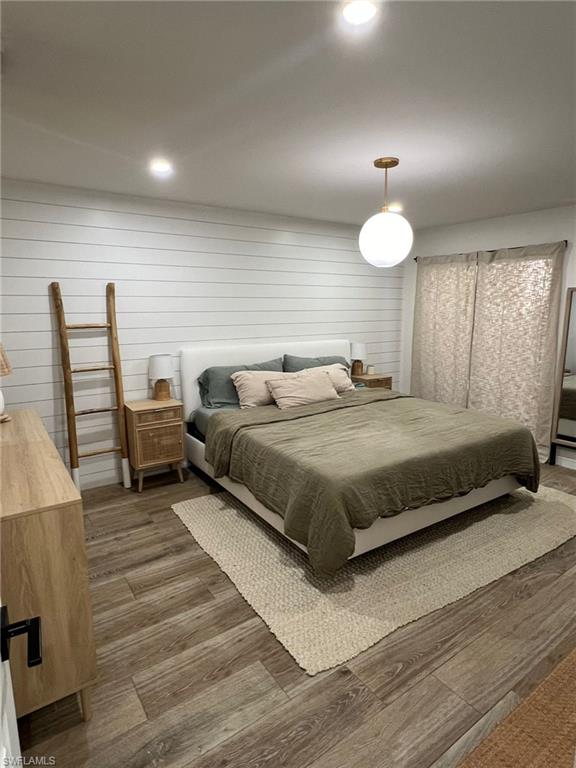 Spacious bedroom featuring wood-finish flooring, a white shiplap accent wall, recessed lighting, and a contemporary globe pendant light fixture
