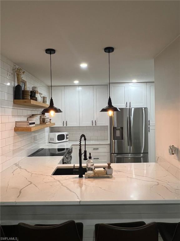 Kitchen featuring a large central island with a black sink and matte black faucet, surrounded by white cabinetry, white subway tile backsplash, and stainless steel appliances