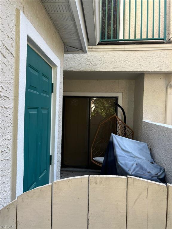 Exterior space featuring a vibrant teal paneled door with white trim, stucco siding, and a partial privacy fence