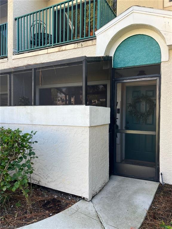 Entryway featuring a teal paneled door with black hardware, textured stucco siding, and tiled flooring