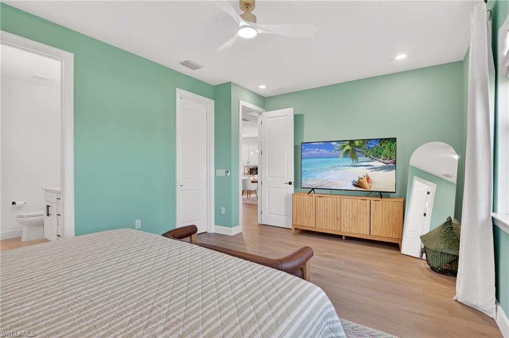 Spacious room with light wood-finish flooring, recessed lighting, a modern ceiling fan, and a white six-panel door leading to a half bath with a white vanity