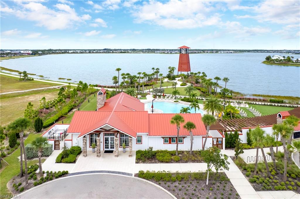 Lakefront community amenity center featuring a red metal roof, a large swimming pool, and a distinctive lighthouse structure