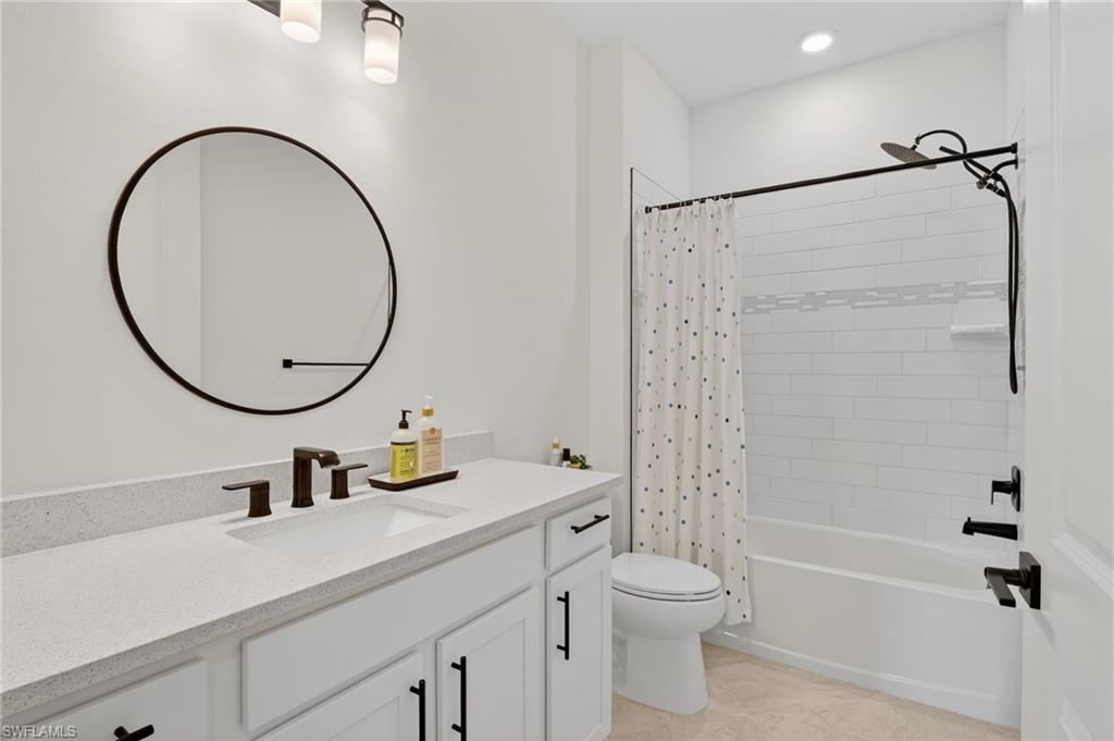 Bathroom featuring a white vanity with a light-toned countertop, a large circular mirror, and matte black fixtures