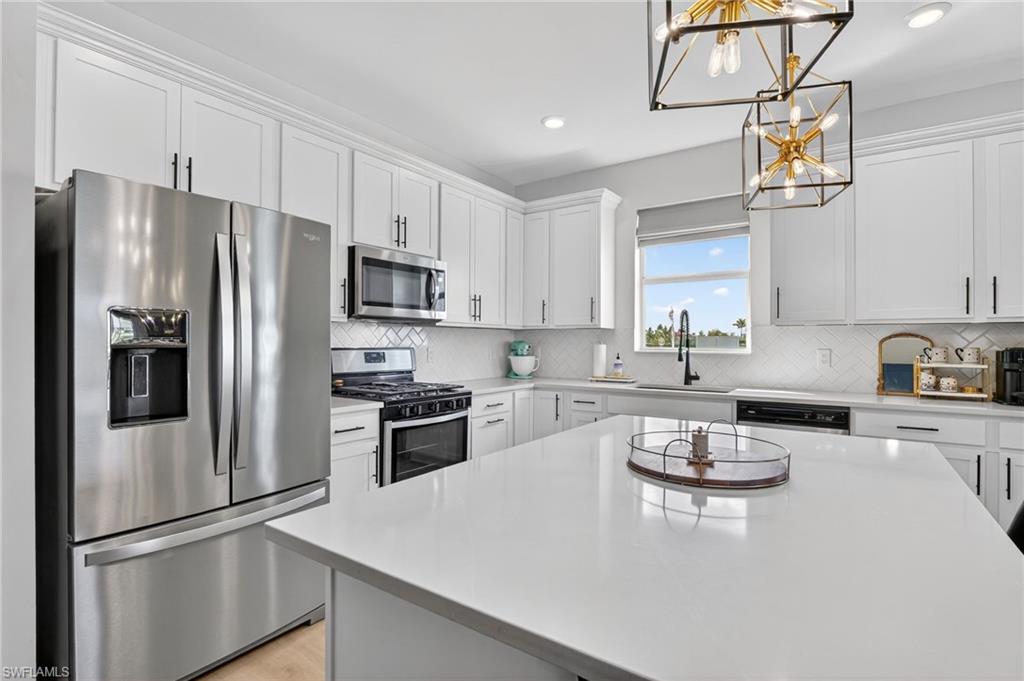 Contemporary kitchen featuring an expansive island with a light-colored countertop, white cabinetry with black hardware, stainless steel appliances, and a diagonal tile backsplash