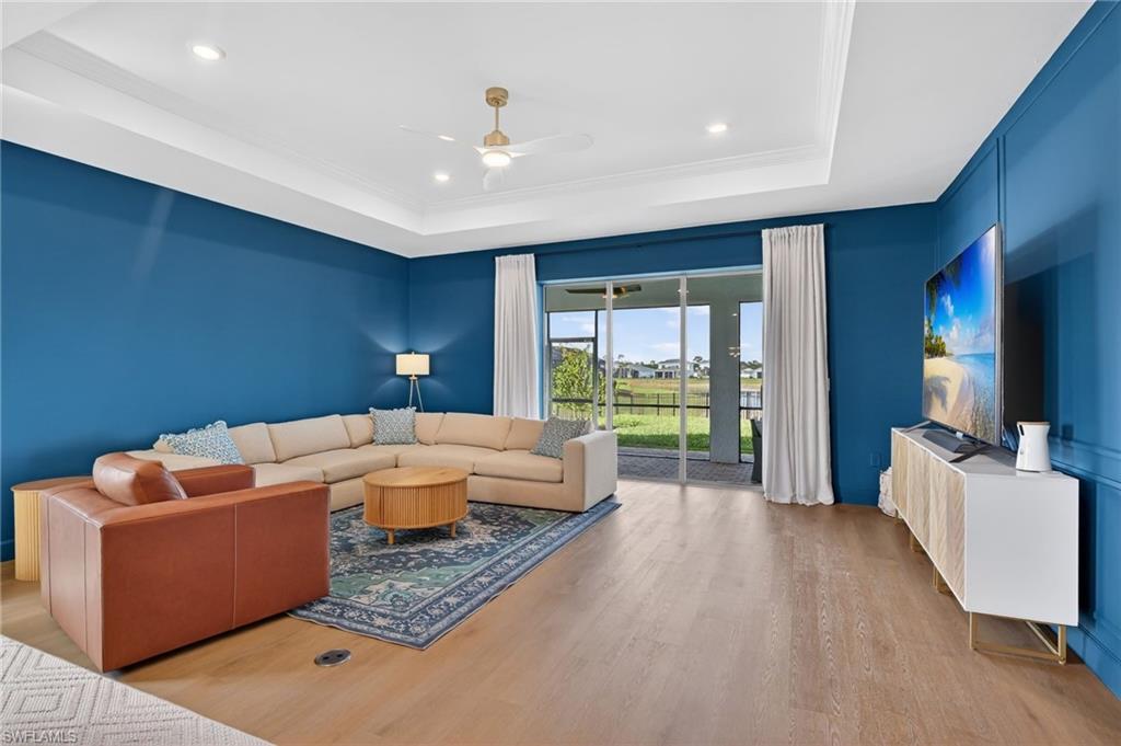 Open-concept living space featuring wood-finish flooring, a tray ceiling with recessed lighting, and a modern ceiling fan