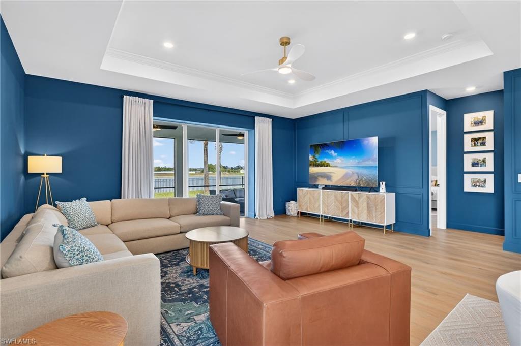 Spacious living area featuring custom wall paneling, light wood-finish flooring, and a tray ceiling with crown molding