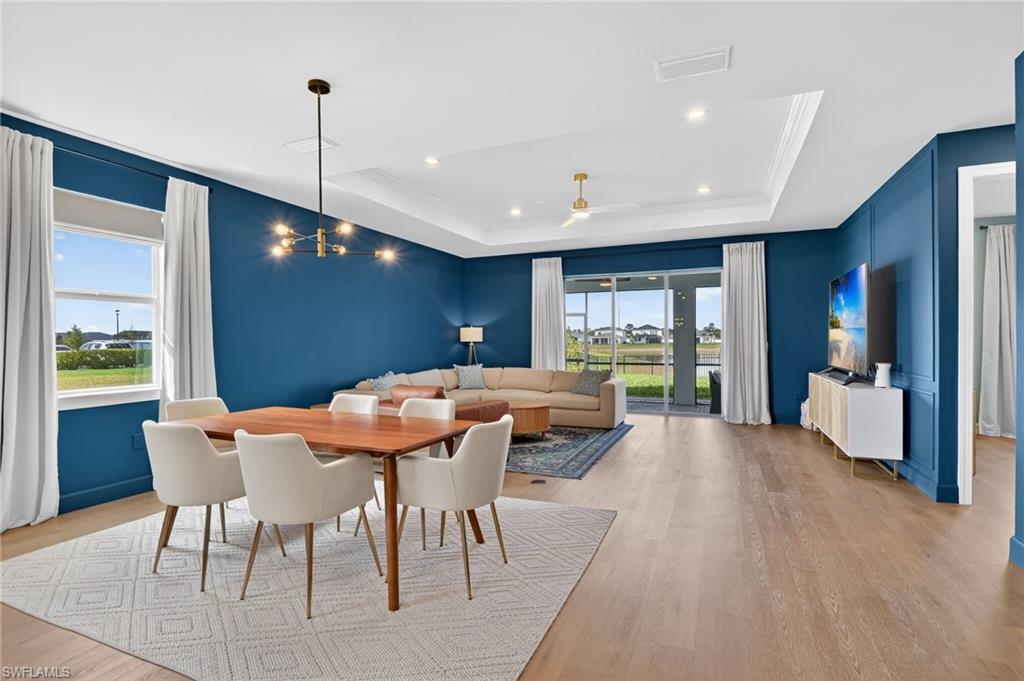 Open concept living area featuring wood-finish flooring, a tray ceiling with recessed lighting, and expansive sliding glass doors leading to a screened lanai