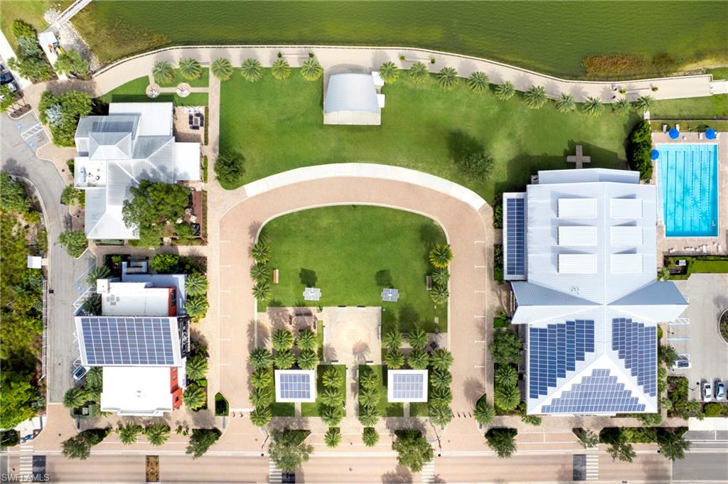 Aerial perspective showcasing multiple properties, extensive green spaces, a large outdoor swimming pool, paved pathways, and numerous solar panels visible on several rooftops