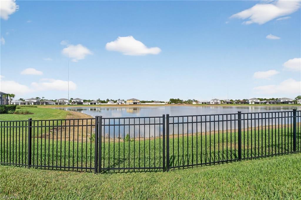 Expansive waterfront property featuring a black metal fence and mature green lawn