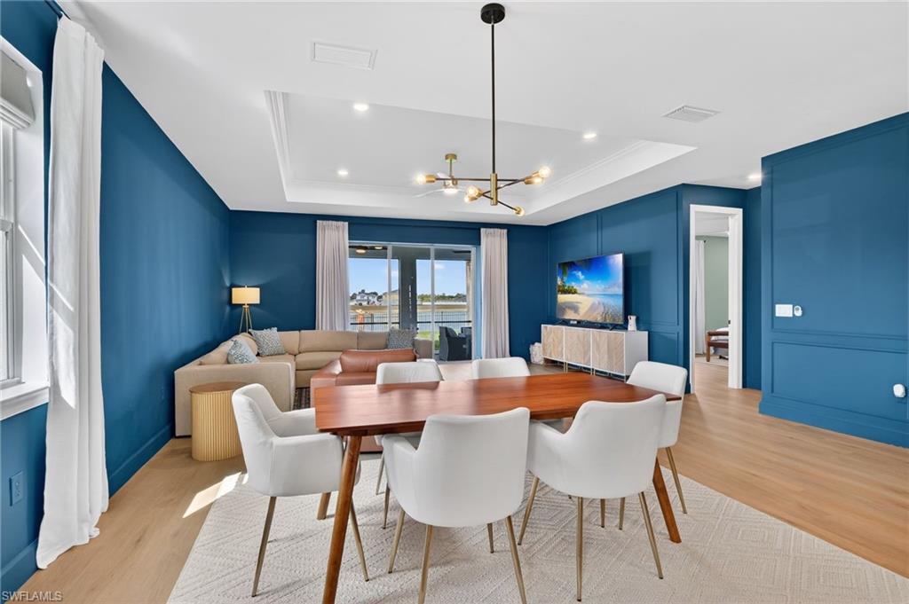 Open-concept living and dining area featuring wood-finish flooring, a tray ceiling with recessed lighting, and a modern chandelier