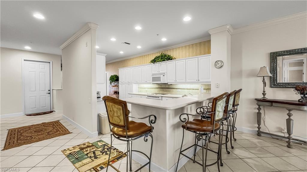 Kitchen featuring white appliances, white cabinets, crown molding, light tile patterned floors, and tasteful backsplash