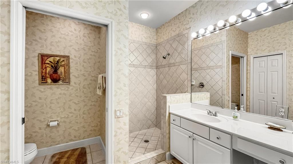 Bathroom with tile patterned flooring, vanity, toilet, and tiled shower