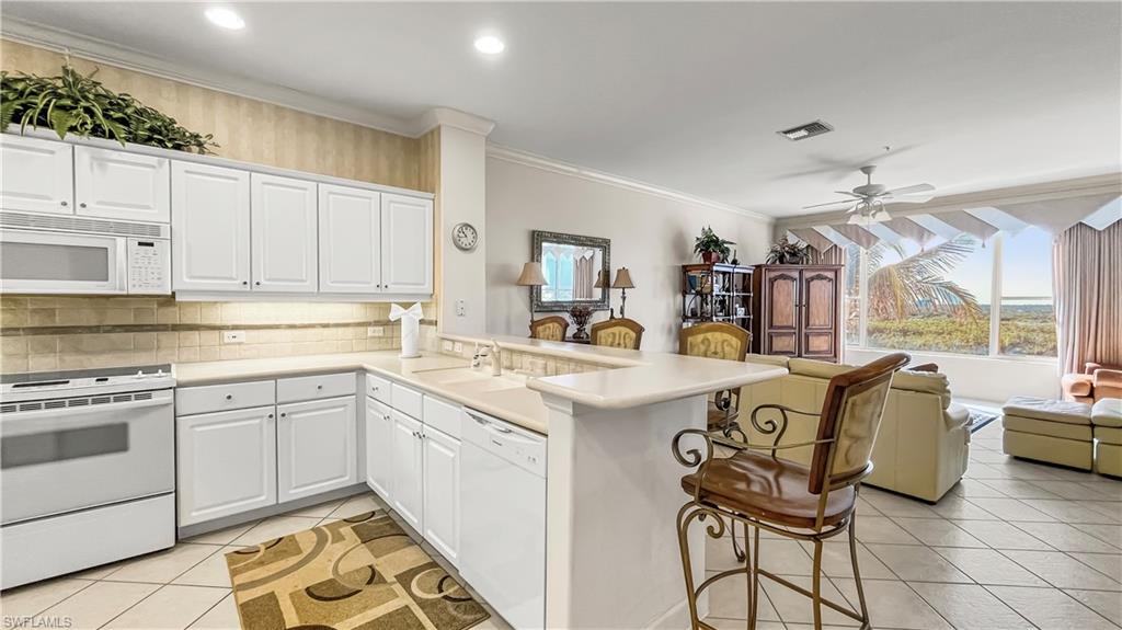 Kitchen with white appliances, white cabinets, light tile patterned floors, a kitchen bar, and kitchen peninsula