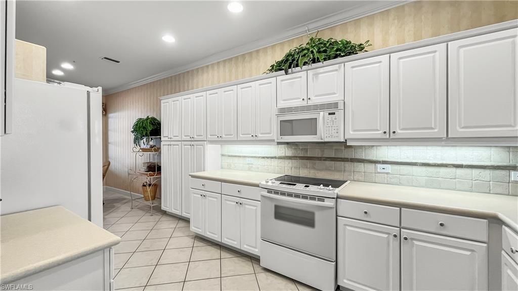 Kitchen with light tile patterned floors, white cabinets, white appliances, and ornamental molding