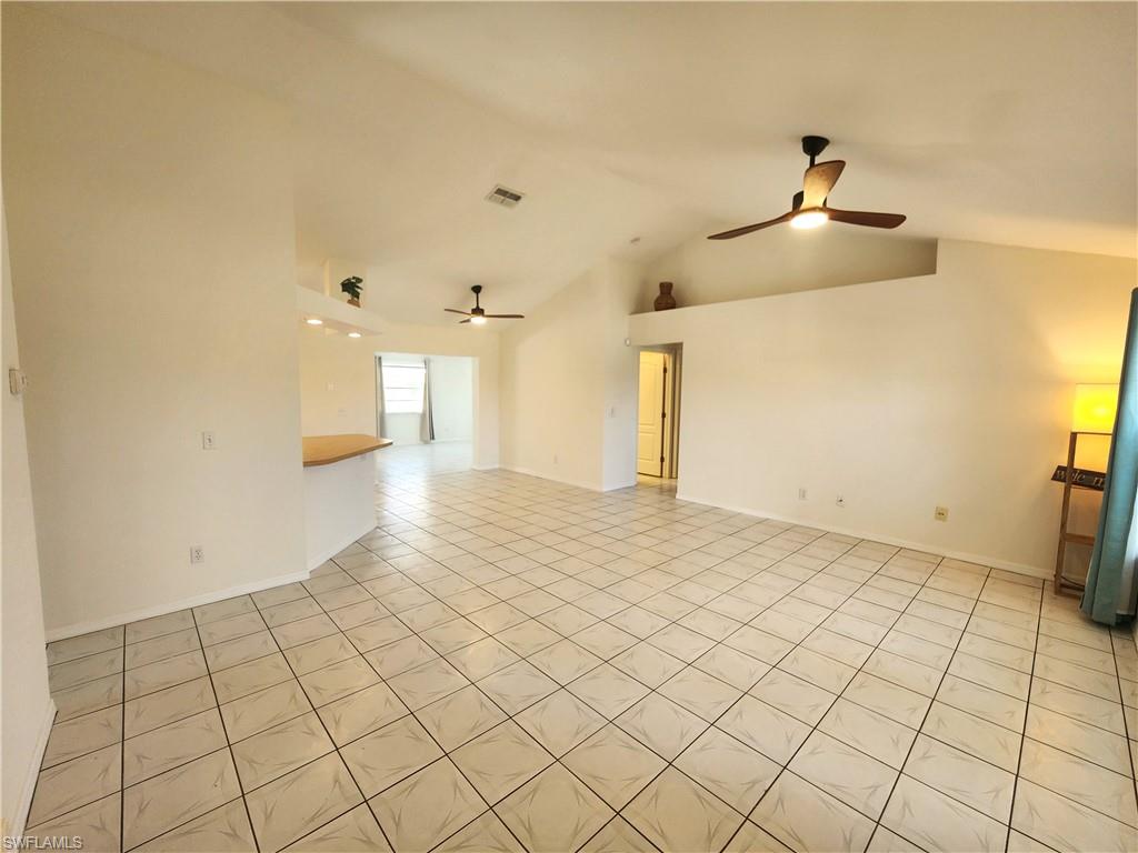 Spacious living area featuring diagonal tile flooring, vaulted ceilings, and two ceiling fans with integrated lighting