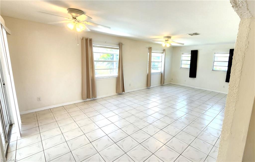 Expansive room featuring white tile flooring, multiple windows, and two ceiling fans with integrated lighting