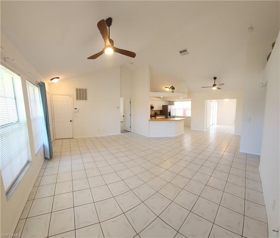 Spacious living area featuring light-toned tile flooring, vaulted ceilings, and multiple windows with blinds