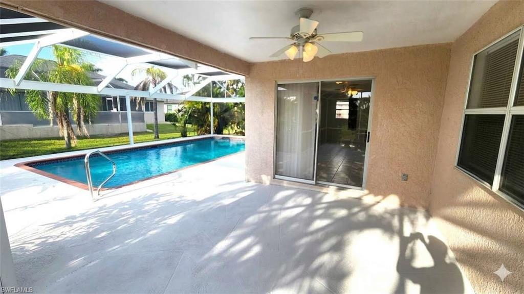 Screened outdoor living area featuring a rectangular pool with a handrail, an expansive patio, and a ceiling fan