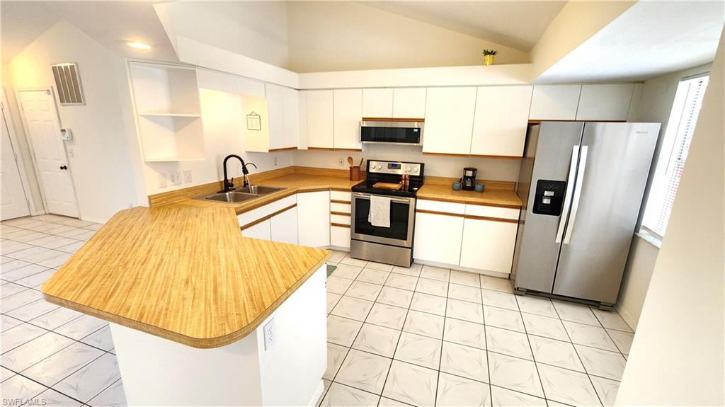 Kitchen featuring a U-shaped island with a wood-finish countertop, white cabinetry, stainless steel appliances, and white tile flooring