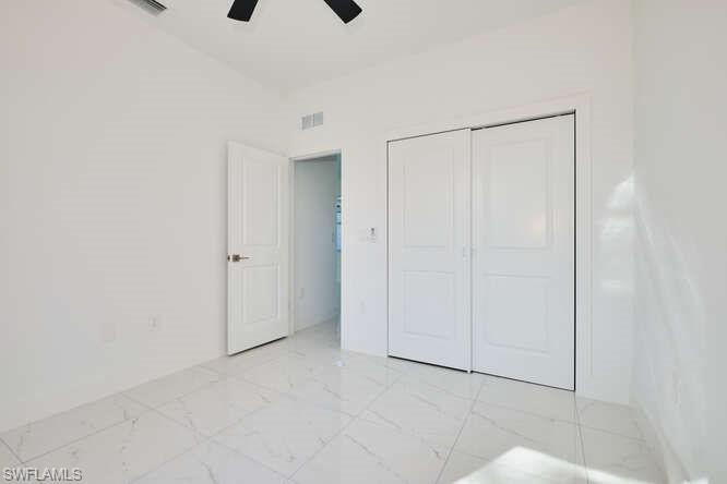Unfurnished bedroom featuring light marble finish flooring, a closet, and ceiling fan