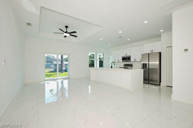 Kitchen featuring open floor plan, stainless steel appliances, white cabinetry, a kitchen island with sink, and a tray ceiling