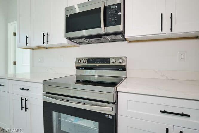Kitchen featuring stainless steel appliances, white cabinetry, and light stone counters