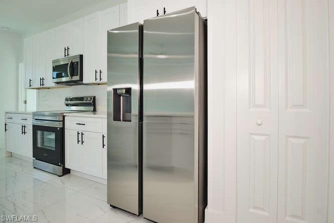 Kitchen featuring stainless steel appliances, white cabinetry, light countertops, and light marble finish flooring