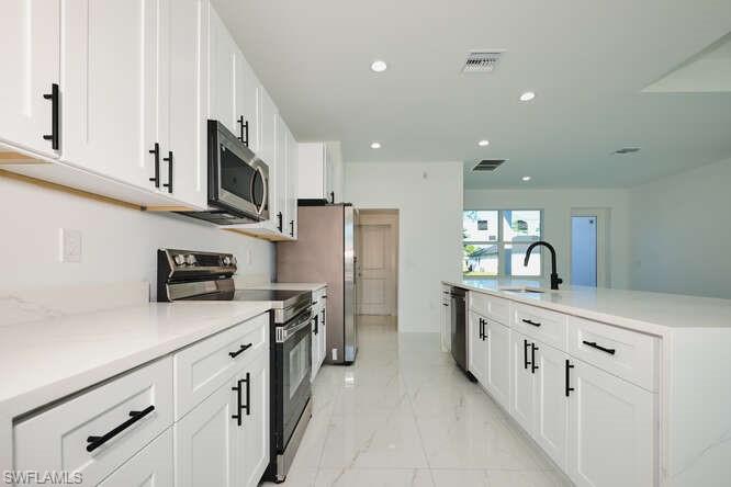 Kitchen with stainless steel appliances, white cabinetry, light marble finish flooring, recessed lighting, and an island with sink
