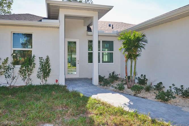 Doorway to property featuring stucco siding and roof with shingles