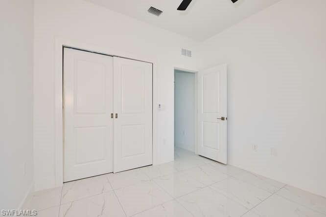 Unfurnished bedroom featuring a closet, light marble finish flooring, and a ceiling fan