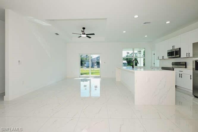 Kitchen with white cabinets, appliances with stainless steel finishes, a center island with sink, light marble finish floors, and recessed lighting