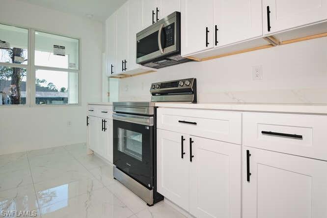 Kitchen featuring appliances with stainless steel finishes, white cabinetry, and light marble finish flooring