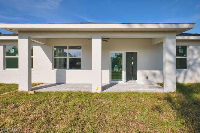 Rear view of property featuring stucco siding, a patio, and a yard