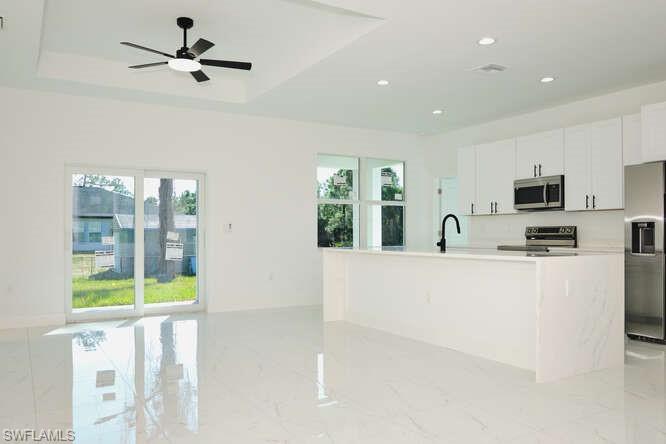 Kitchen with appliances with stainless steel finishes, white cabinets, an island with sink, light marble finish flooring, and recessed lighting