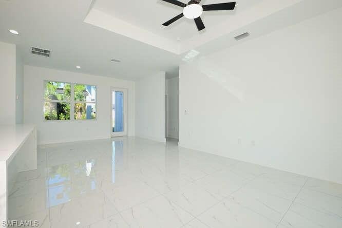 Empty room with a raised ceiling, light marble finish flooring, and ceiling fan