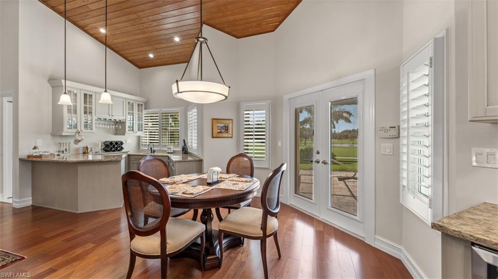 Open-concept dining space with wood-finish flooring, a vaulted wood-plank ceiling, and a built-in wet bar featuring upper glass-front cabinetry and pendant lighting