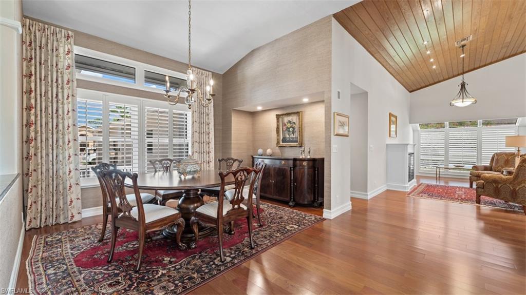 Dining area featuring vaulted ceilings with wood-finish paneling, hardwood flooring, and a chandelier