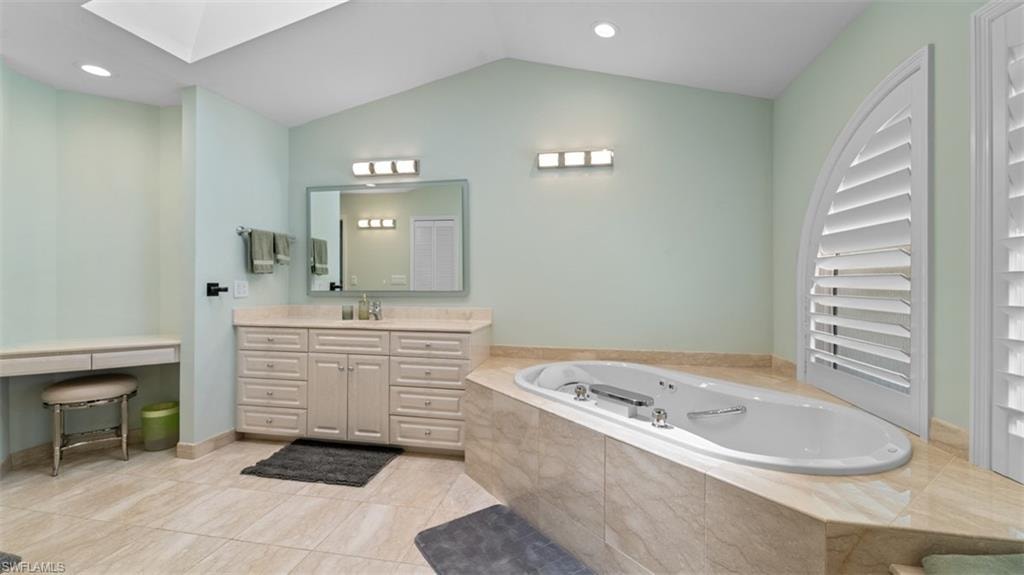 Spa-inspired bathroom featuring a jetted tub set in a stone surround, a dual vanity with ample storage, a dedicated vanity desk, and arched louvered window treatments