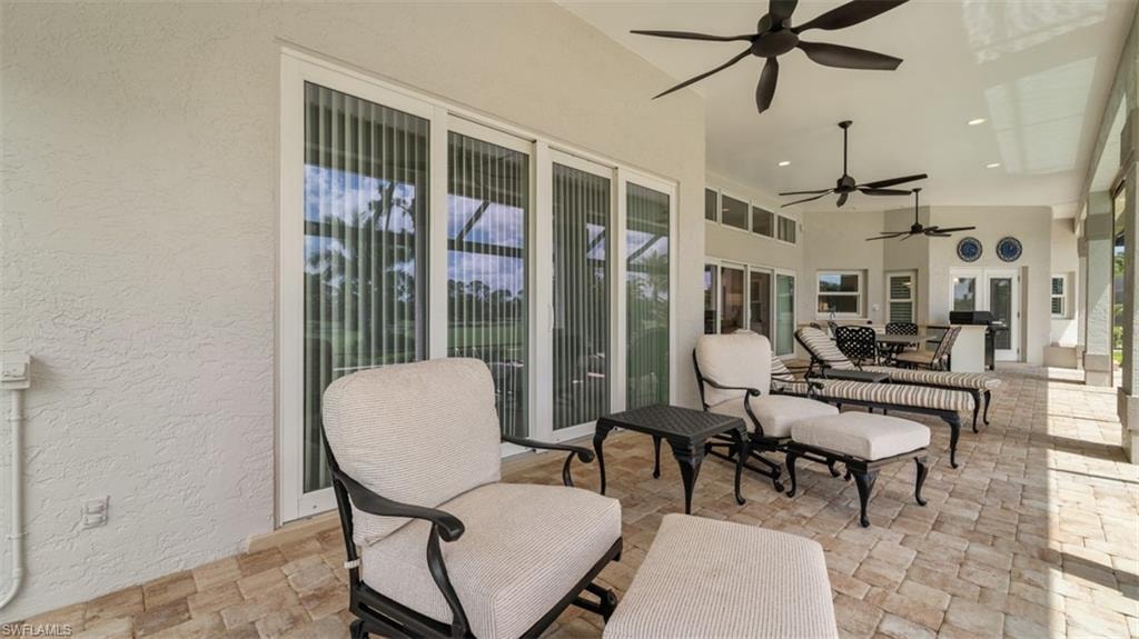 Expansive covered patio featuring a paver floor, multiple ceiling fans, and sliding glass doors
