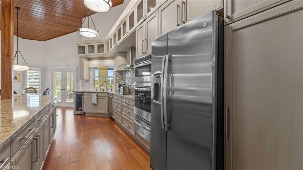 Gourmet kitchen featuring stainless steel appliances, extensive cabinetry with glass-front uppers, granite countertops, wood-finish flooring, and a vaulted wood-paneled ceiling