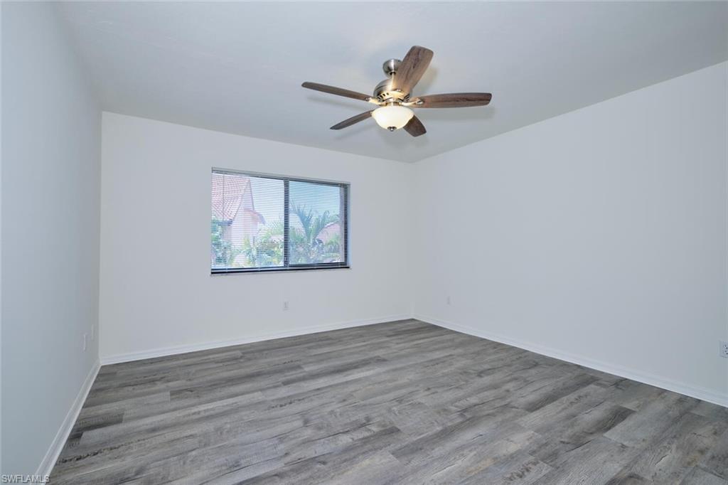 Spacious room featuring wood-finish flooring, a ceiling fan with integrated lighting, and a window providing natural illumination