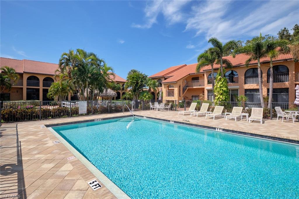 Rectangle swimming pool surrounded by paver decking, featuring a black metal fence and lush palm trees