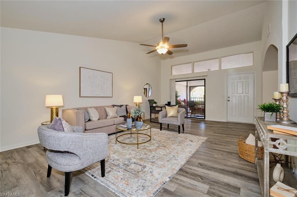Spacious living area featuring vaulted ceilings, wood-finish flooring, a ceiling fan with integrated lighting, and a sliding glass door providing exterior access