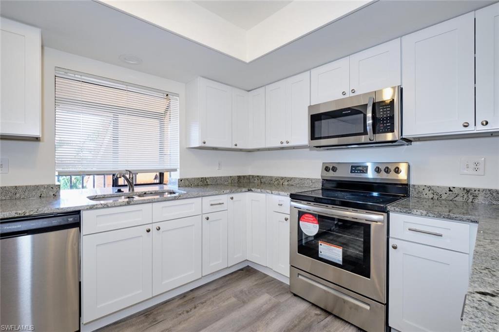 Kitchen with stone countertops, stainless steel appliances, wood-finish flooring, and a window with blinds