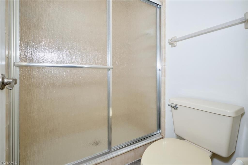 Shower enclosure with textured glass doors, brushed nickel handle, and a tan toilet
