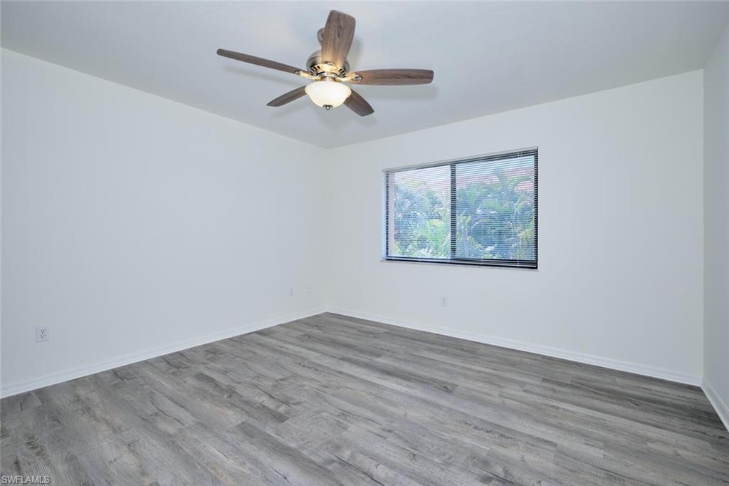 Room featuring light gray wood-finish flooring, white walls, a window with dark trim, and a ceiling fan with integrated lighting