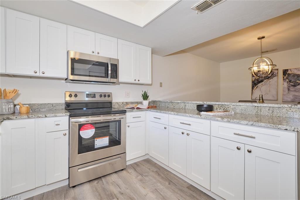 Kitchen featuring white shaker cabinetry, stainless steel appliances, speckled countertops, and wood-finish flooring