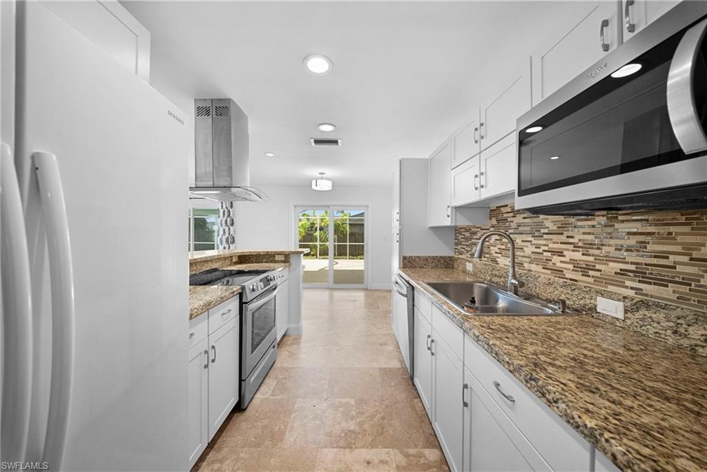 Modern kitchen featuring white cabinetry, stainless steel appliances, a mosaic tile backsplash, and granite countertops