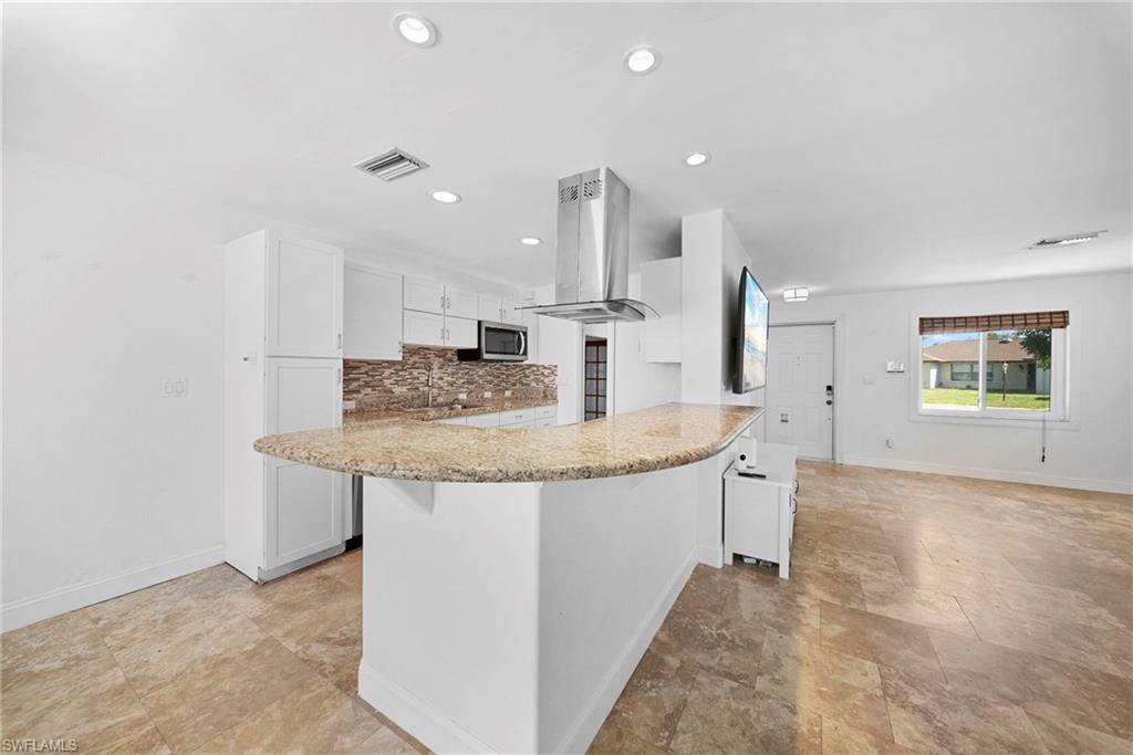 Modern kitchen featuring white cabinetry, a large peninsula with a stone countertop, an integrated microwave, and a stainless steel range hood